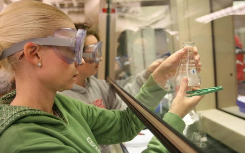students in a lab wearing goggles and holding a beaker containing liquid