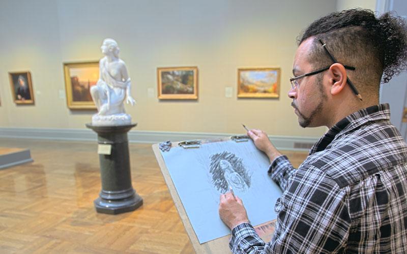 man at an easle stand studies and sketches the statue in front of him