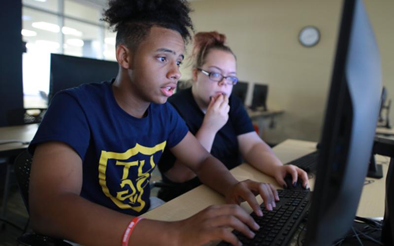 two students sitting in a computer lab share a computer screen