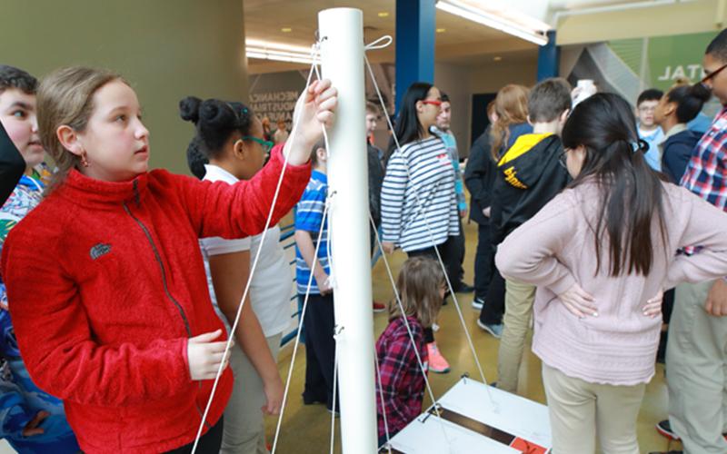 young students fill an auditorium and one pulls at rope connected to a white pole 