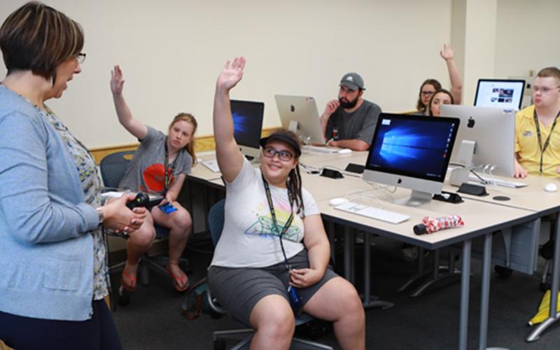 students sitting in a computer lab raise their hand to be chosen by the teacher