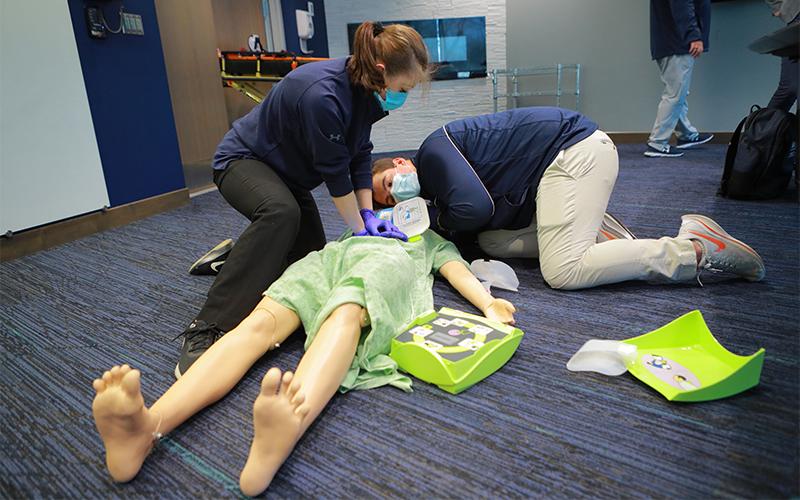 two students practice CPR procedures on a mannequin