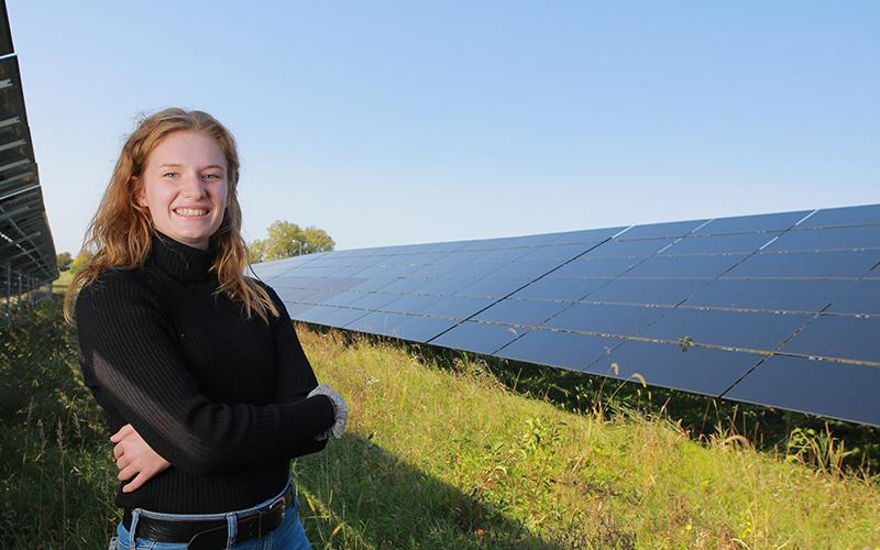 woman in a field stands in front of a row of solar panels