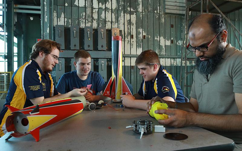 engineering students sit at a table assembling a rocket