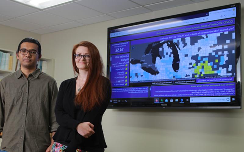 two students stand in front of a screen displaying geographic map data