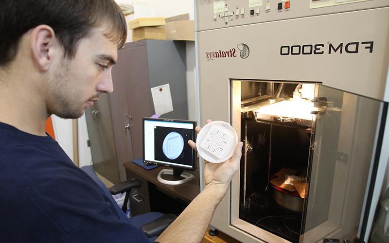 man observes a circular white disc removed from a piece of lab machinery