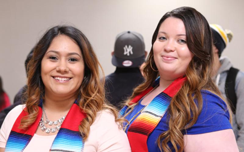 two students smile while wearing tri-colored Latin American sashes