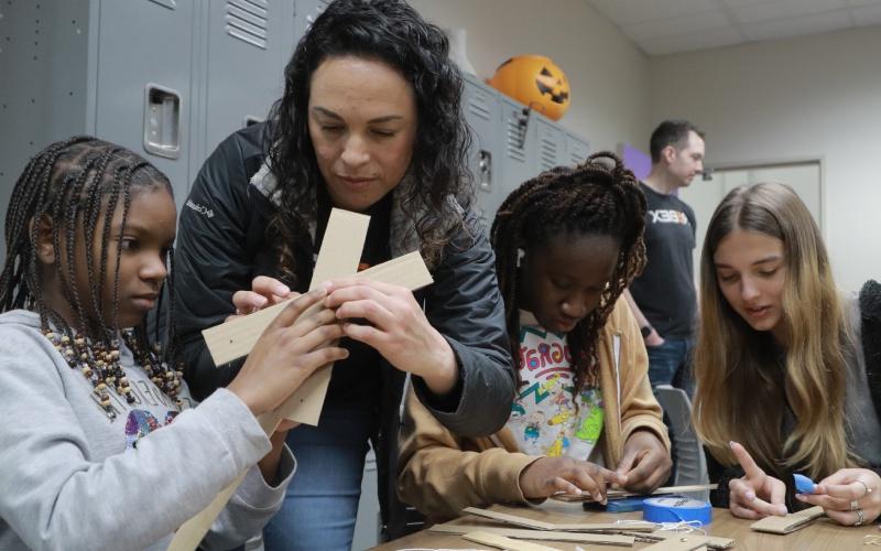 teacher helps assemble a craft along three students