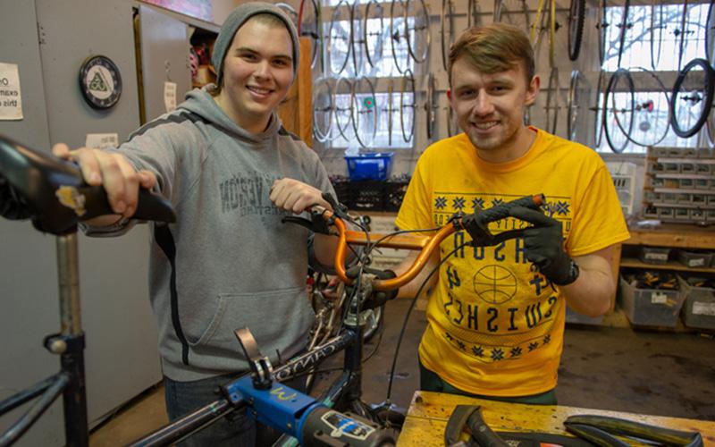 two students smile and stand together in a repair workshop
