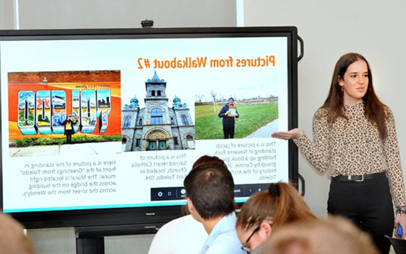 woman presents powerpoint on screen to a group 