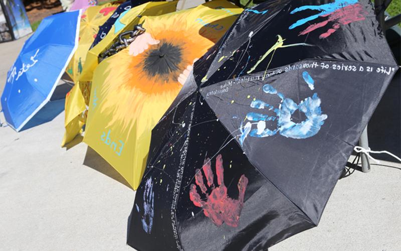 umbrellas lined up on the ground, one is black with colorful handprints