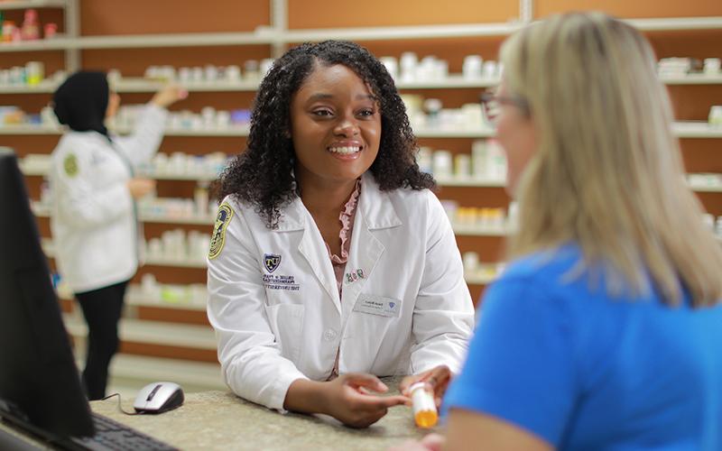 pharmacist hands over an orange prescription bottle to patient