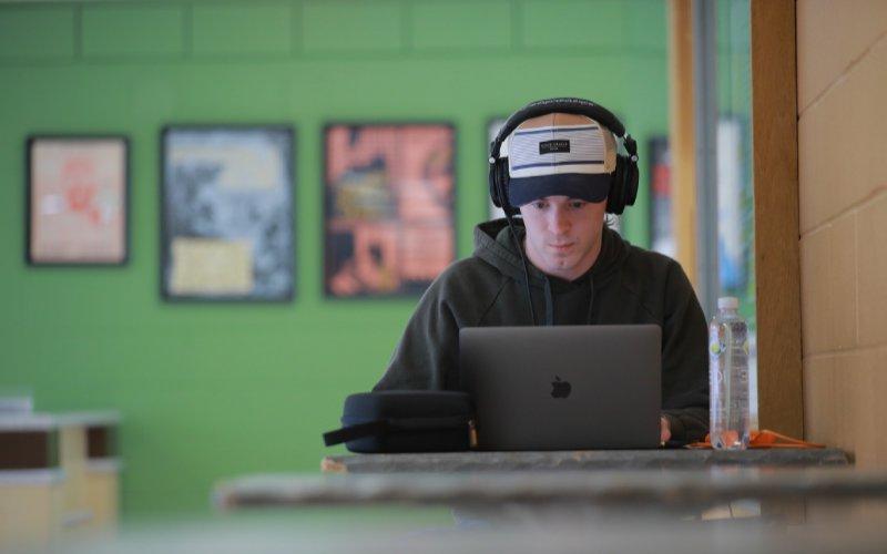 student wearing headphones focuses and looks down at open laptop